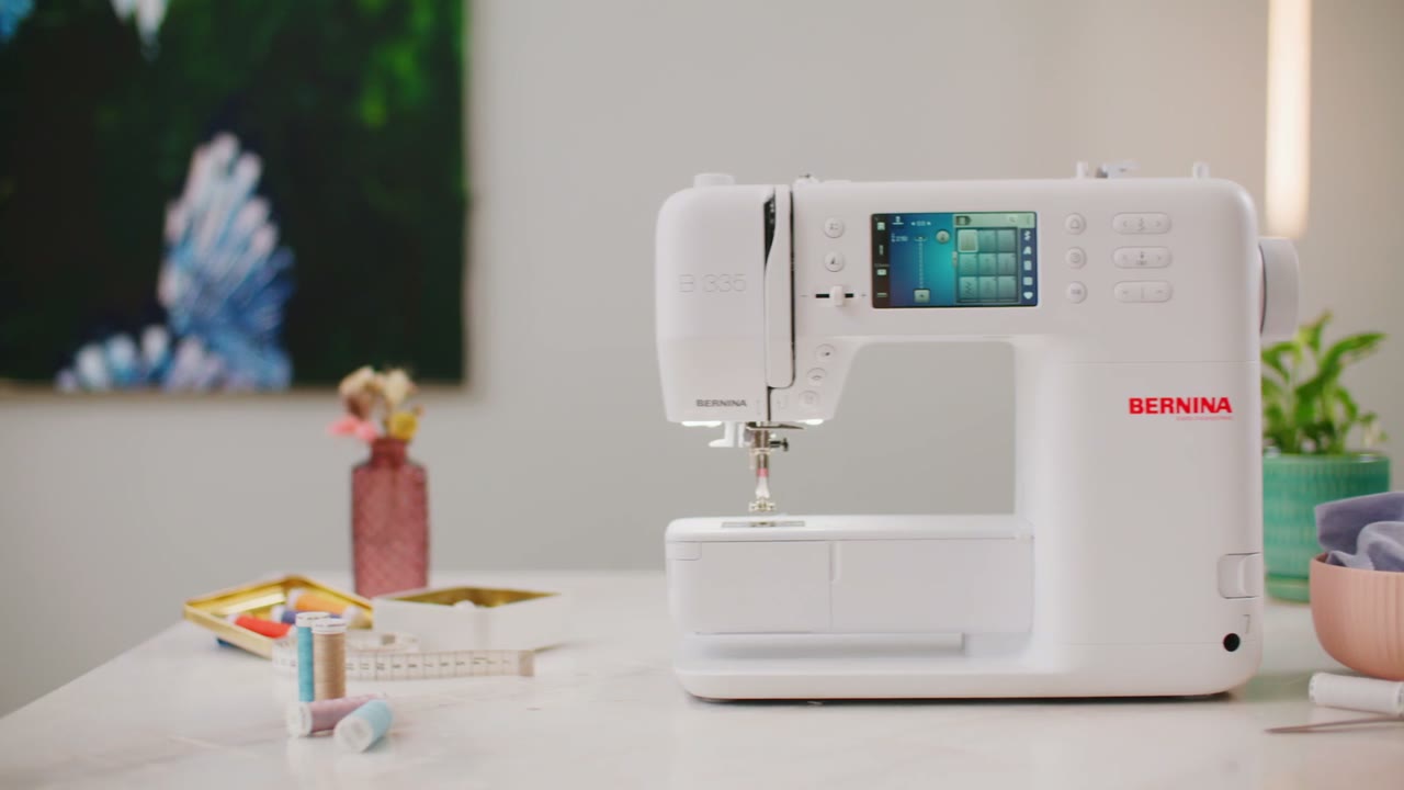 Szene aus dem Produktfilm BERNINA 3 Series: eine weiße BERNINA-Nähmaschine auf einem hellen Tisch mit Garnrollen