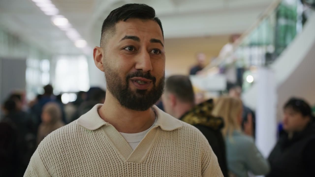 Szene aus dem Veranstaltungsfilm Messe Future Together: ein Mann im Interview in einer vollen Messehalle