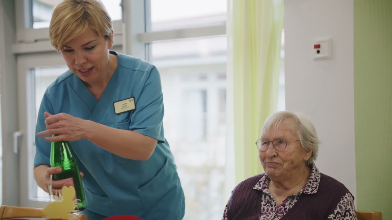 Szene aus dem Regionalfilm Paderborn: eine Pflegekraft schenkt einer älteren Dame Wasser ein