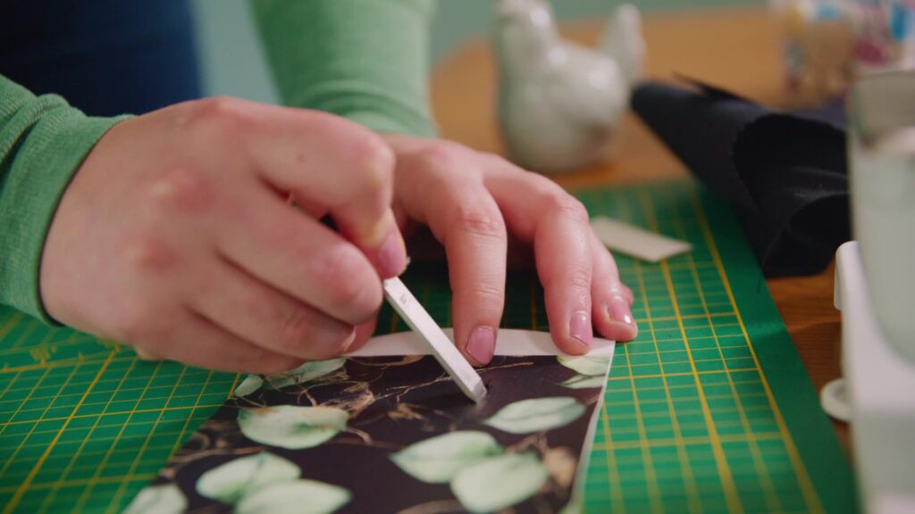 Hands mark the leaf-patterned fabric on the green cutting mat