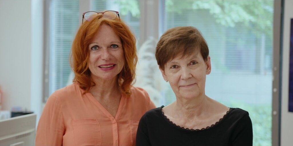 Two smiling women look into the camera in the bright office