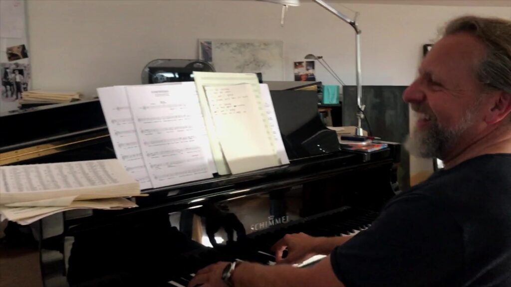 Komponist spielt lachend Klavier mit Notenblättern im Studio