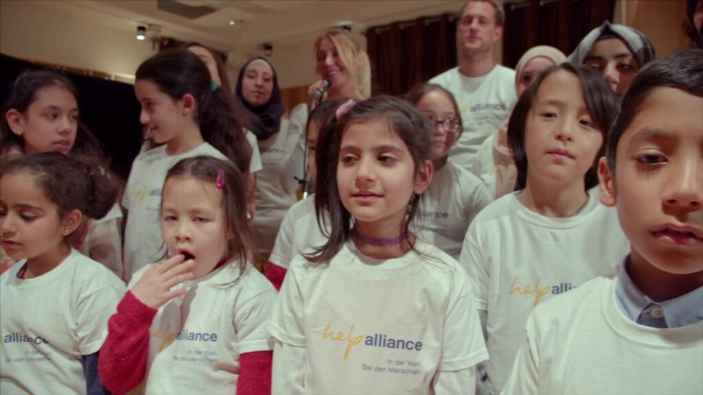 Singende Kinder im Chor mit help-alliance-Shirts beim Konzert