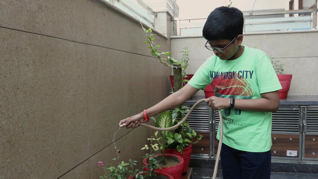 Boy waters the potted plants on the terrace with a hose