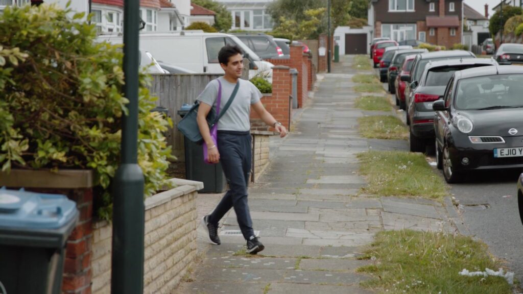 Young man with a shoulder bag walks along a quiet residential street