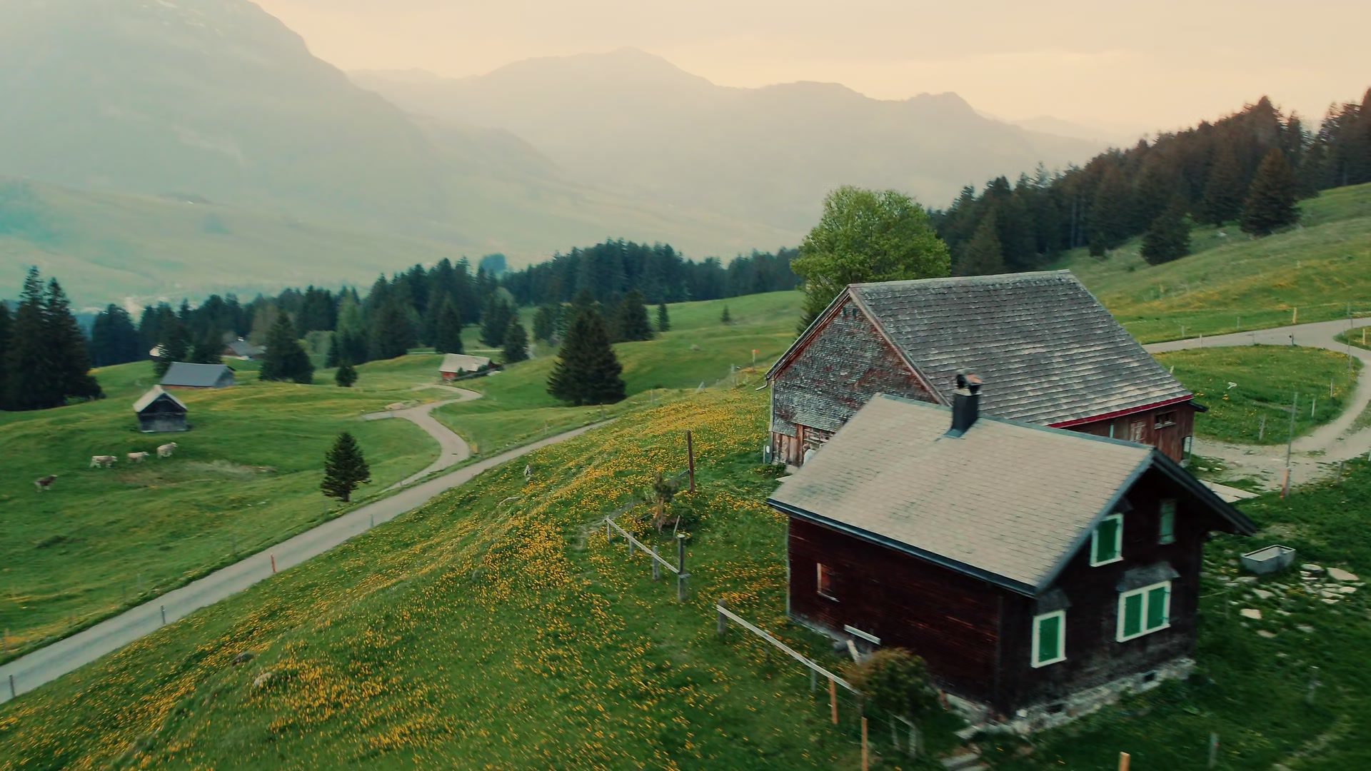 Traditional farm on a green alpine meadow in front of misty mountains