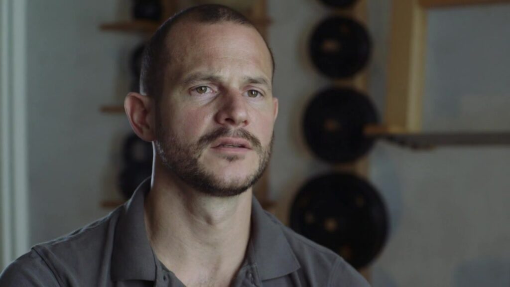 Portrait of a trainer in front of a wall with weights