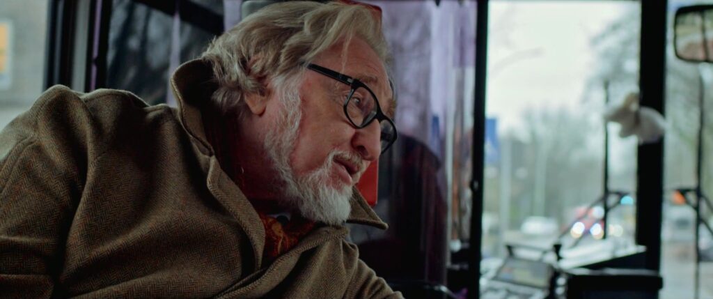 Older man with glasses and scarf on the bus, in profile