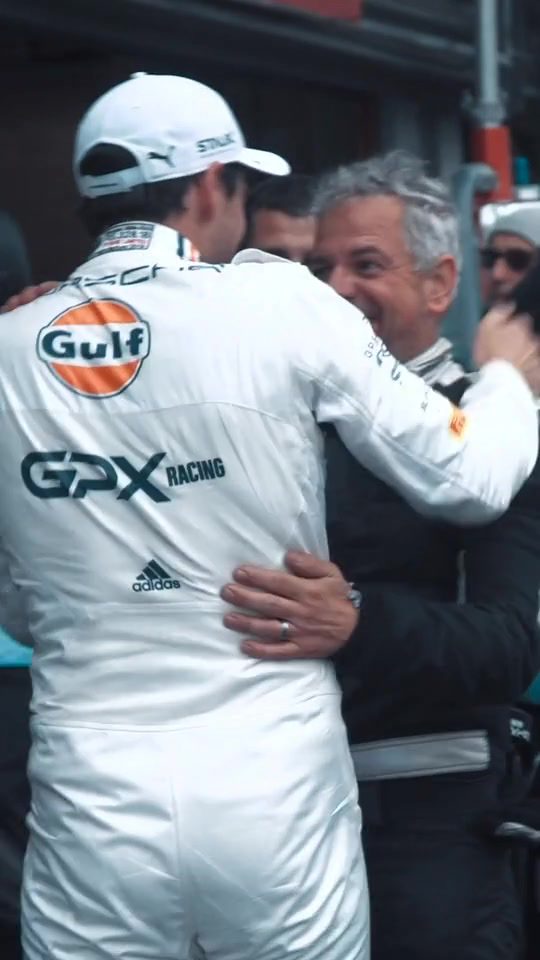 Rennfahrer im Gulf-Overall umarmt lachend ein Teammitglied nach dem Rennen
