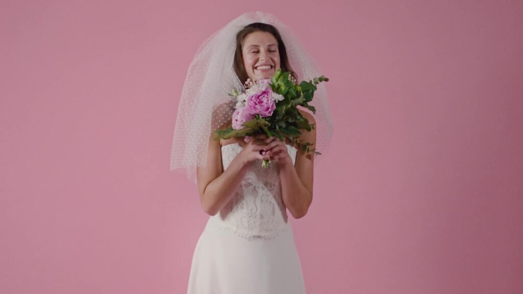 Laughing bride with veil and pink bridal bouquet against a pink background
