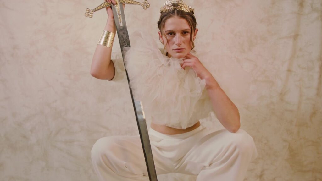 Model with crown and sword in tulle fashion against a pink background