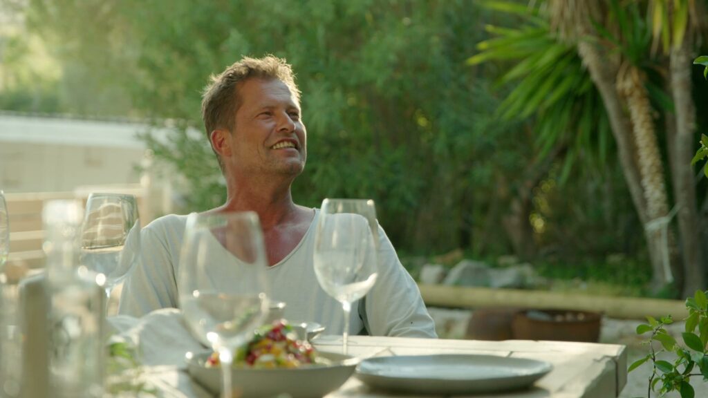 Til Schweiger sitzt entspannt an der gedeckten Tafel im Garten der Finca.