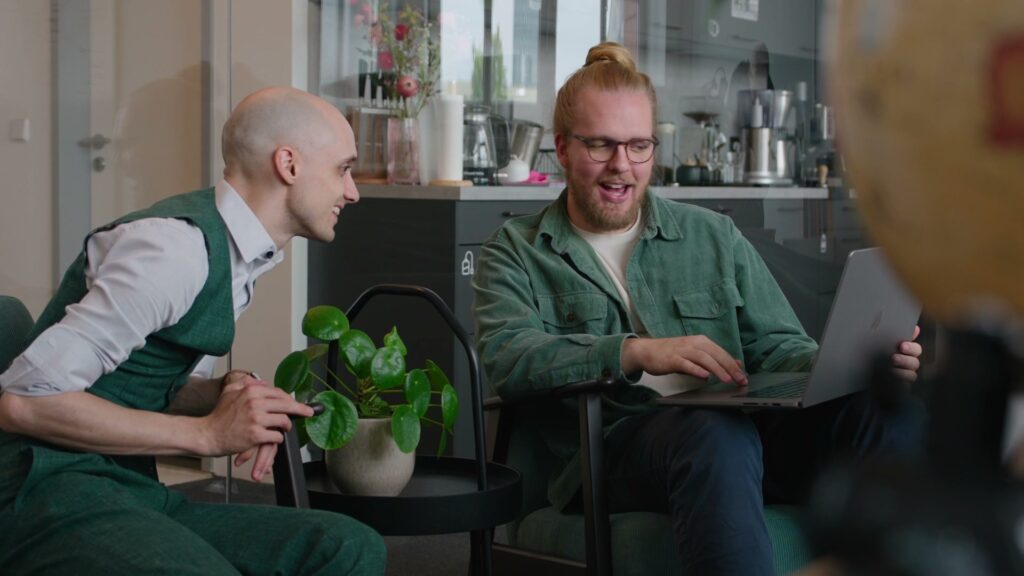 Zwei Mitarbeiter von Berlin Bytes lachen bei einer kurzen Abstimmung am Laptop in der Bürokueche