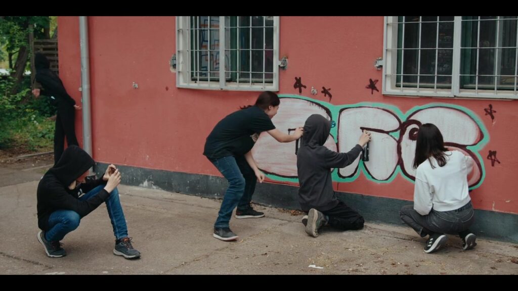 Jugendliche sprühen gemeinsam ein Graffiti an eine Hauswand