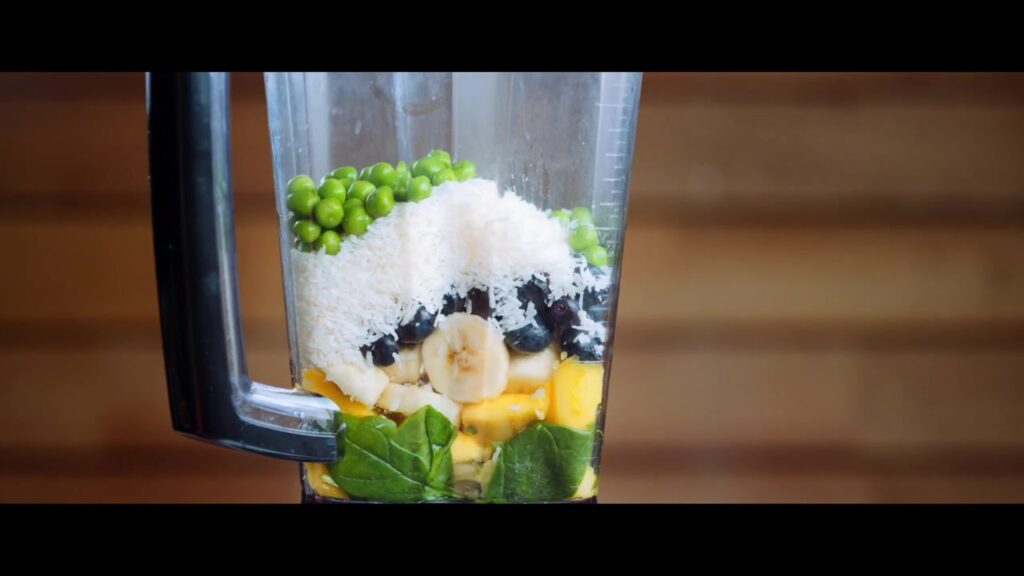 Mixer gefüllt mit Erbsen, Kokosraspeln, Blaubeeren, Banane und Spinat