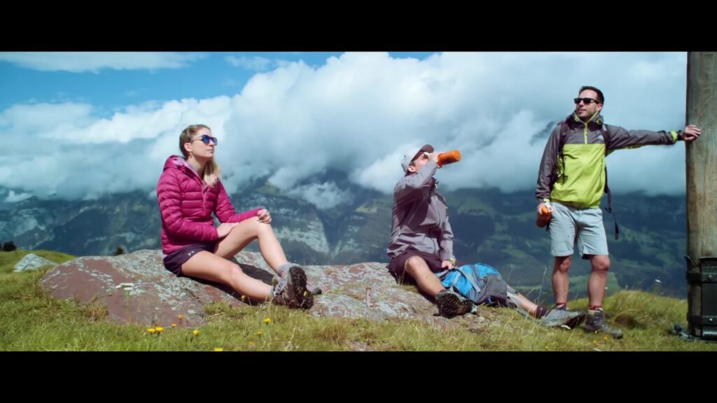 Drei Wanderer rasten auf dem Gipfel und trinken FOOCH-Smoothie