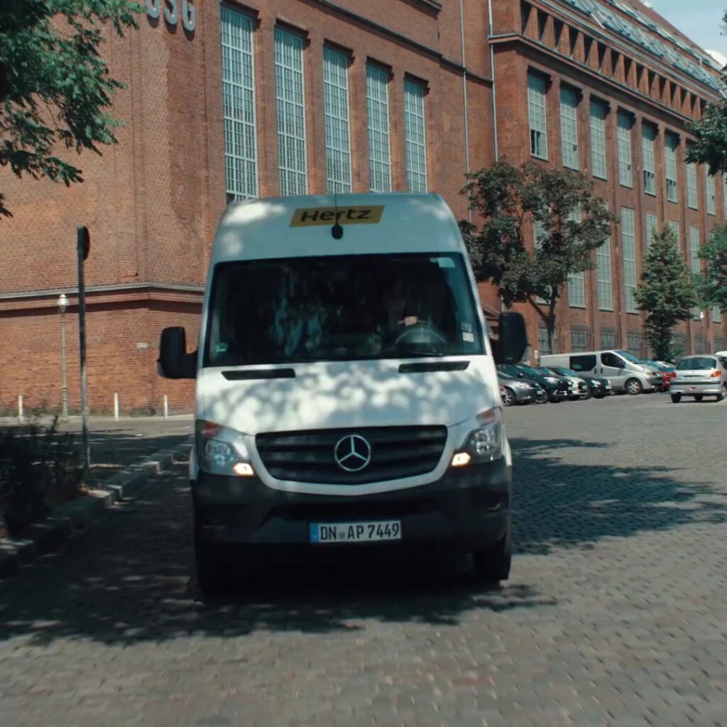 Weißer Hertz-Transporter fährt über Kopfsteinpflaster vor Berliner Backsteinfassade
