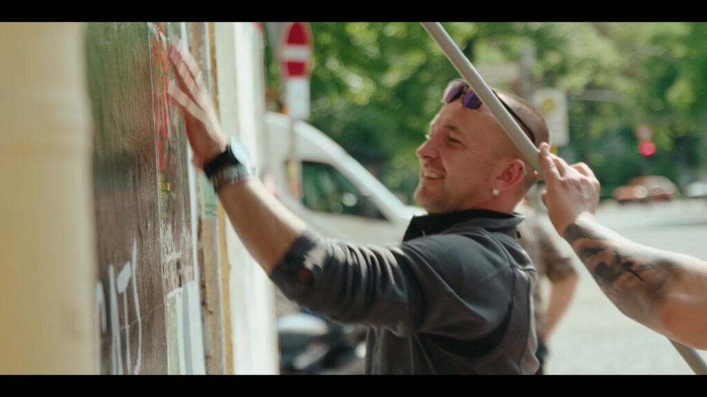 Lächelnder Plakatierer klebt ein Plakat an eine Wand im Sonnenlicht