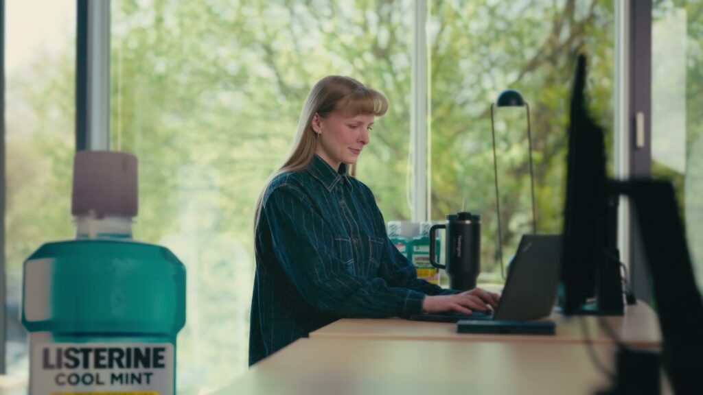 Hannah arbeitet am Laptop an ihrem Schreibtisch, daneben eine Listerine-Flasche und weitere Kenvue-Marken.