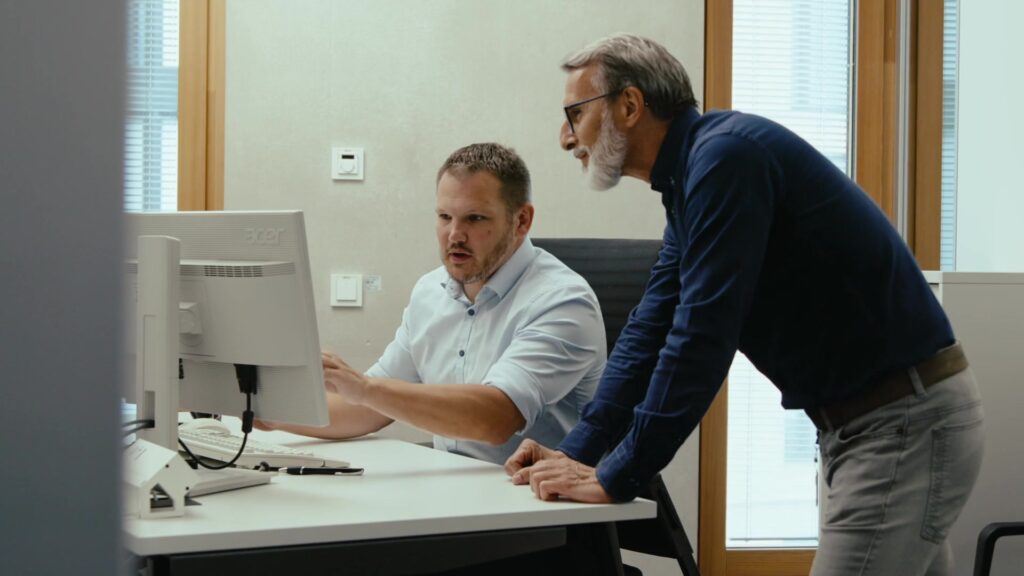 Zwei Kollegen besprechen Softwareprozesse gemeinsam am Computer im Büro