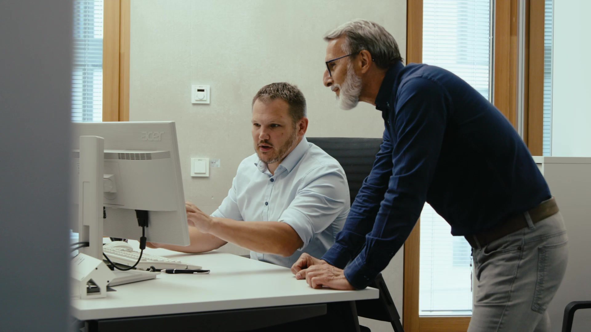 Two colleagues discuss software processes at the computer in the office