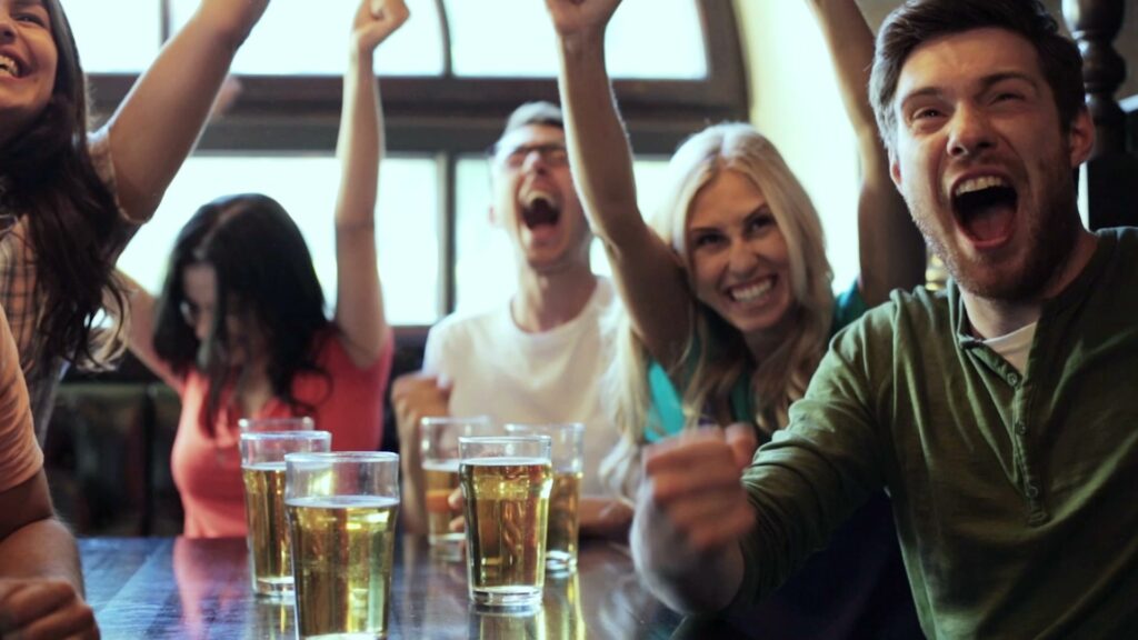 Freunde jubeln beim Tor in einer Bar mit Bier auf dem Tresen.