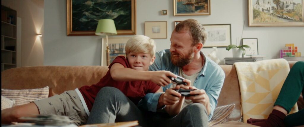Vater und Sohn spielen zusammen ein Videospiel auf der Couch.