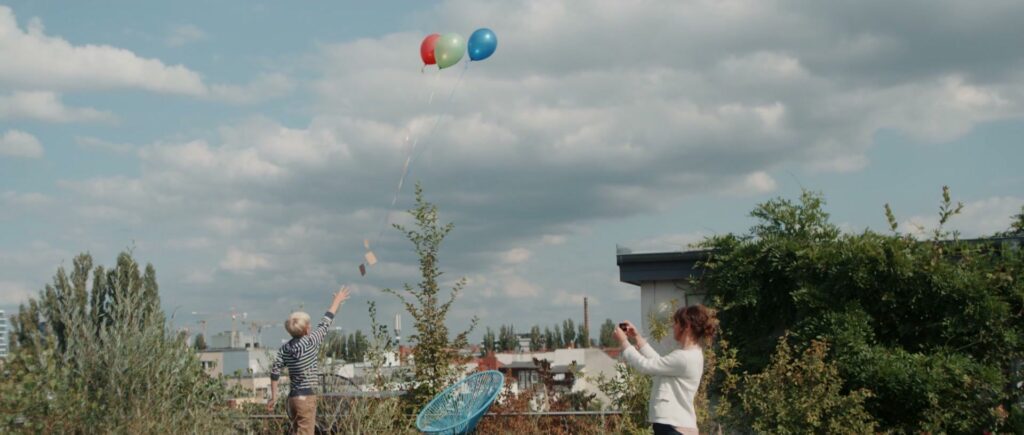 Familie lässt Luftballons mit Wunschkarten von der Dachterrasse steigen.