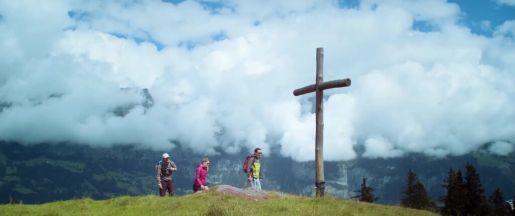 Wanderer erreichen ein Gipfelkreuz vor dramatischer Wolkenkulisse