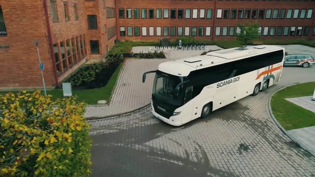 Weißer Scania-Reisebus fährt über einen Campus mit Backsteingebäuden