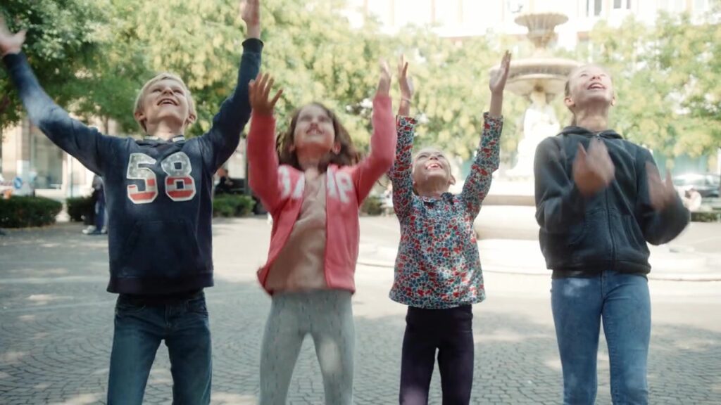 Vier Kinder jubeln mit erhobenen Armen auf einer Piazza